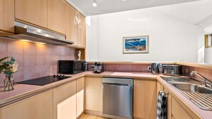 A compact kitchen with wooden cabinets, a stainless steel dishwasher, a microwave, a toaster, and a coffee maker.