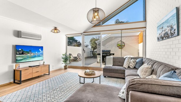 A spacious living room with a large TV, comfortable seating, a dining area, and a sliding glass door leading to an outdoor space.