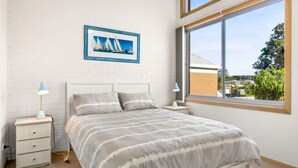 A bedroom with a bed, two bedside tables, a window with a view, and a framed picture on the wall.