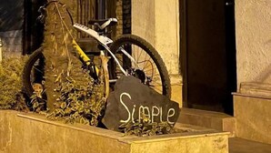 Een fiets geparkeerd naast een palmboom en een steen met de tekst 'Simple', voor een gebouw met een deur waarop 'Simple' staat.