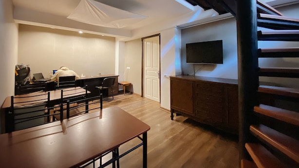 Een moderne woonkamer met houten vloer, een eettafel, een bank, een aan de muur bevestigde televisie en een trap.