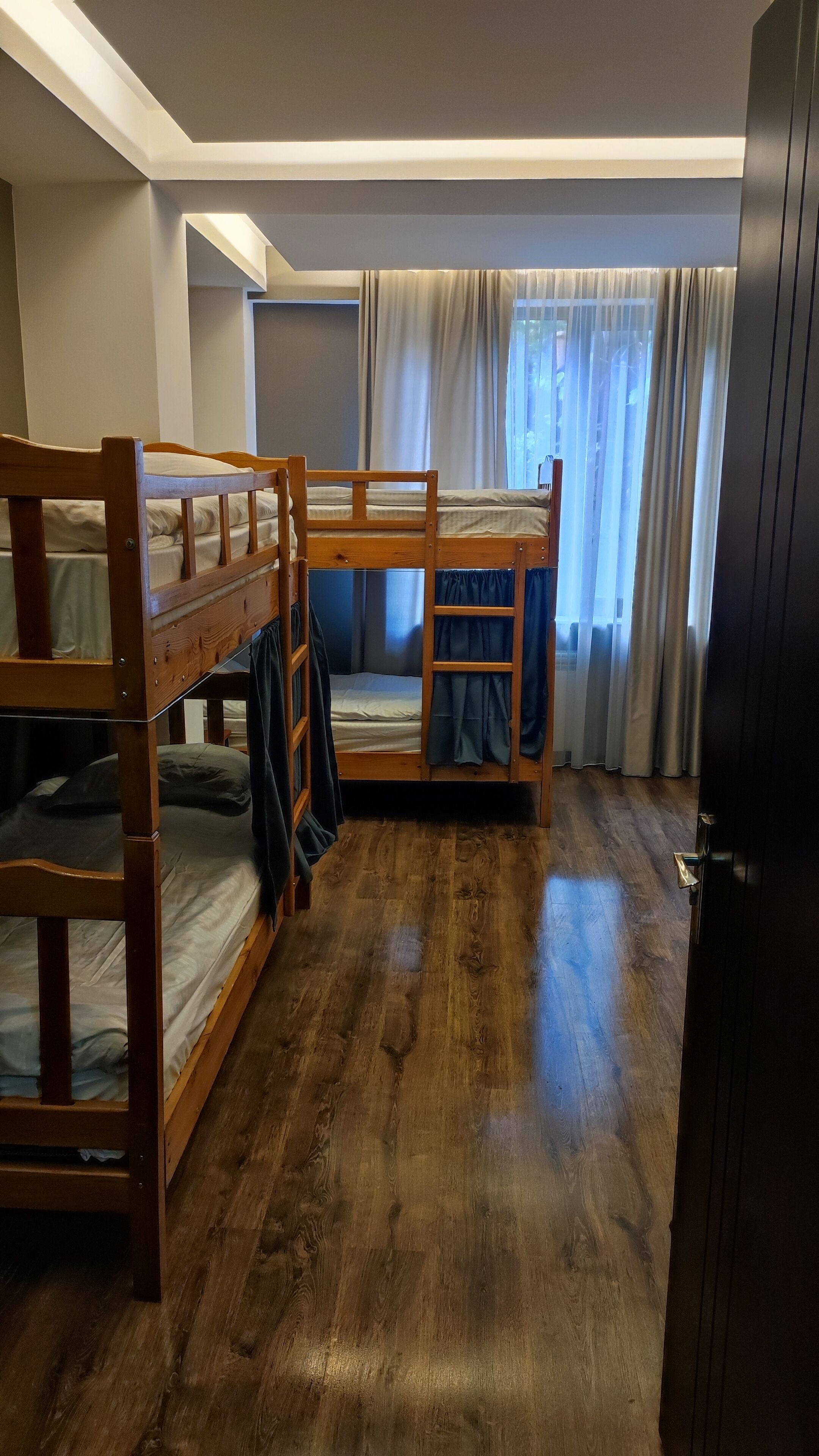 Een kamer met stapelbedden, houten vloer en een raam met gordijnen.