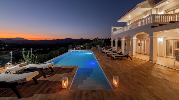 Un espace aménagé au bord de la piscine, avec des chaises longues et une vue sur les montagnes au coucher du soleil.