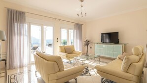 Un salon moderne avec un canapé, des fauteuils, une table basse en verre, un téléviseur à écran plat et une vue dégagée grâce à de grandes fenêtres.