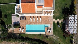 Vue aérienne d’une propriété dotée d’une piscine, de chaises longues, d’un patio et d’un jardin.