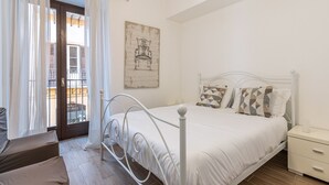Ein Schlafzimmer mit einem weißen Bett, einem Nachttisch, einem Sessel und Blick auf den Balkon.