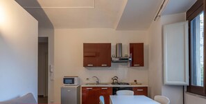 A compact kitchen with a microwave, stove, and cabinets. There's a dining table with chairs and a sofa in the living area.