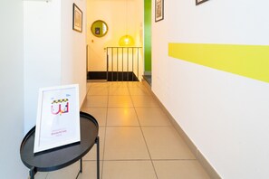 A hallway with a framed welcome sign, a round mirror, and a yellow stripe on the wall.