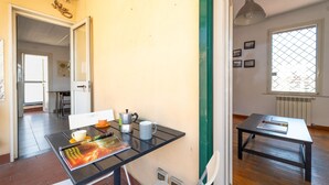 A room with a dining table, chairs, a coffee pot, a mug, and a book. There is a window with a view of buildings outside. - Stylish in Spanish Quarter by Wonderful Italy (Napoli)