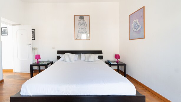 A hotel room with a large bed, two bedside tables, a door, and two framed artworks on the walls. - Stylish in Spanish Quarter by Wonderful Italy (Napoli)