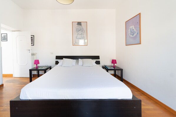 A hotel room with a large bed, two bedside tables, a door, and two framed artworks on the walls.