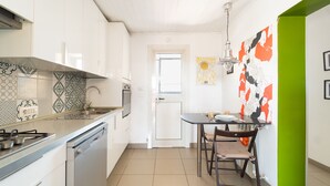 A modern kitchen with white cabinets, a gas stove, and a dishwasher. There's a dining table with chairs and a wall with abstract art. - Stylish in Spanish Quarter by Wonderful Italy (Napoli)
