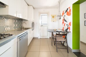 A modern kitchen with white cabinets, a gas stove, and a dishwasher. There's a dining table with chairs and a wall with abstract art.
