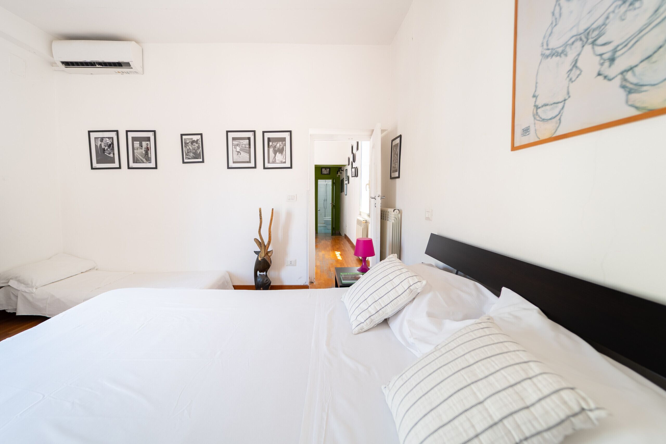 Une chambre d’hôtel comprenant un lit, une table de chevet, une lampe et un climatiseur fixé au mur.