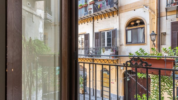 A view through a window of a building with balconies, a wrought iron fence, and a door with a gate. - Casa Borsa con Balcone by Wonderful Italy (Palermo)