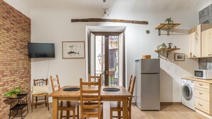 A compact kitchen with a dining area, a washing machine, and a TV mounted on the wall. - Casa Borsa con Balcone by Wonderful Italy (Palermo)