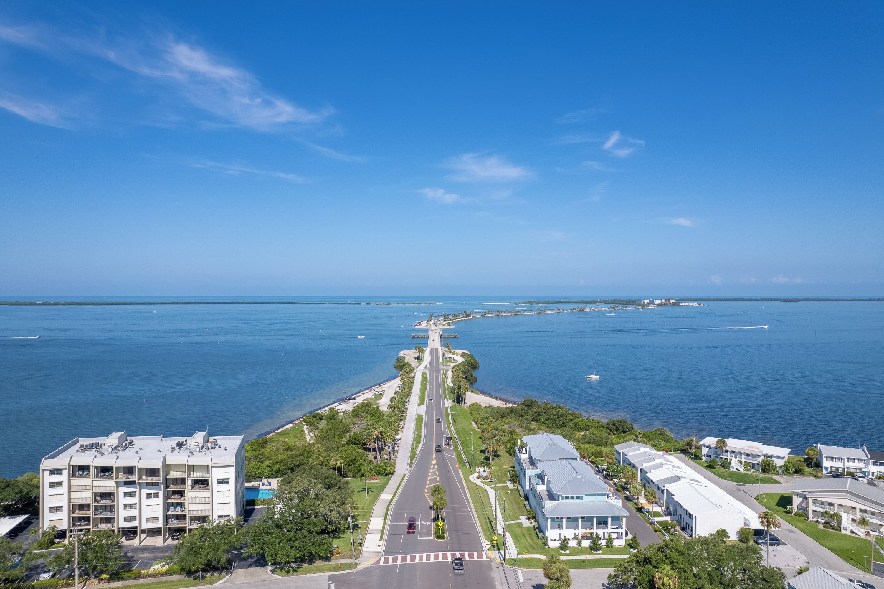 A coastal road with a clear view of the ocean, lined with buildings and greenery.