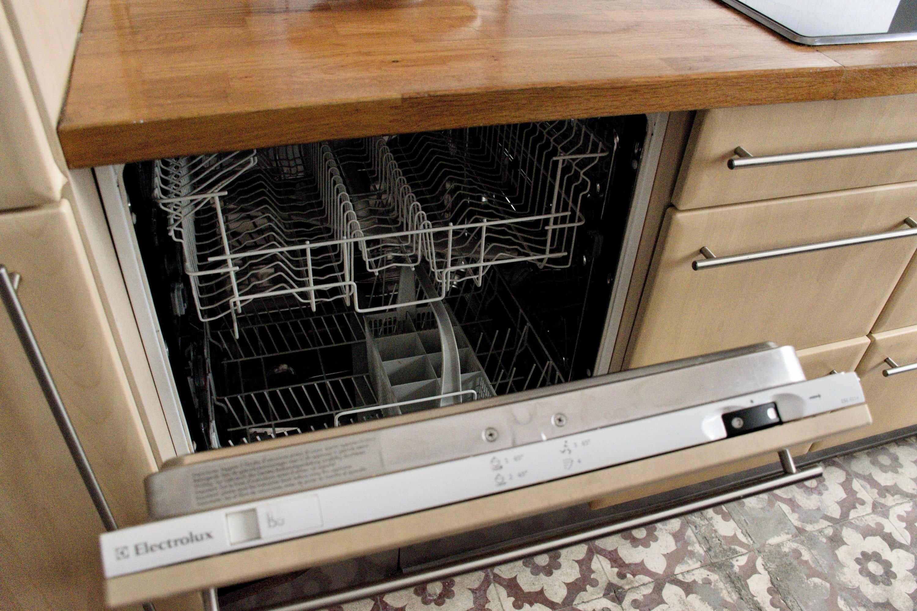 A dishwasher with a control panel, a wooden countertop above it, and a patterned floor.