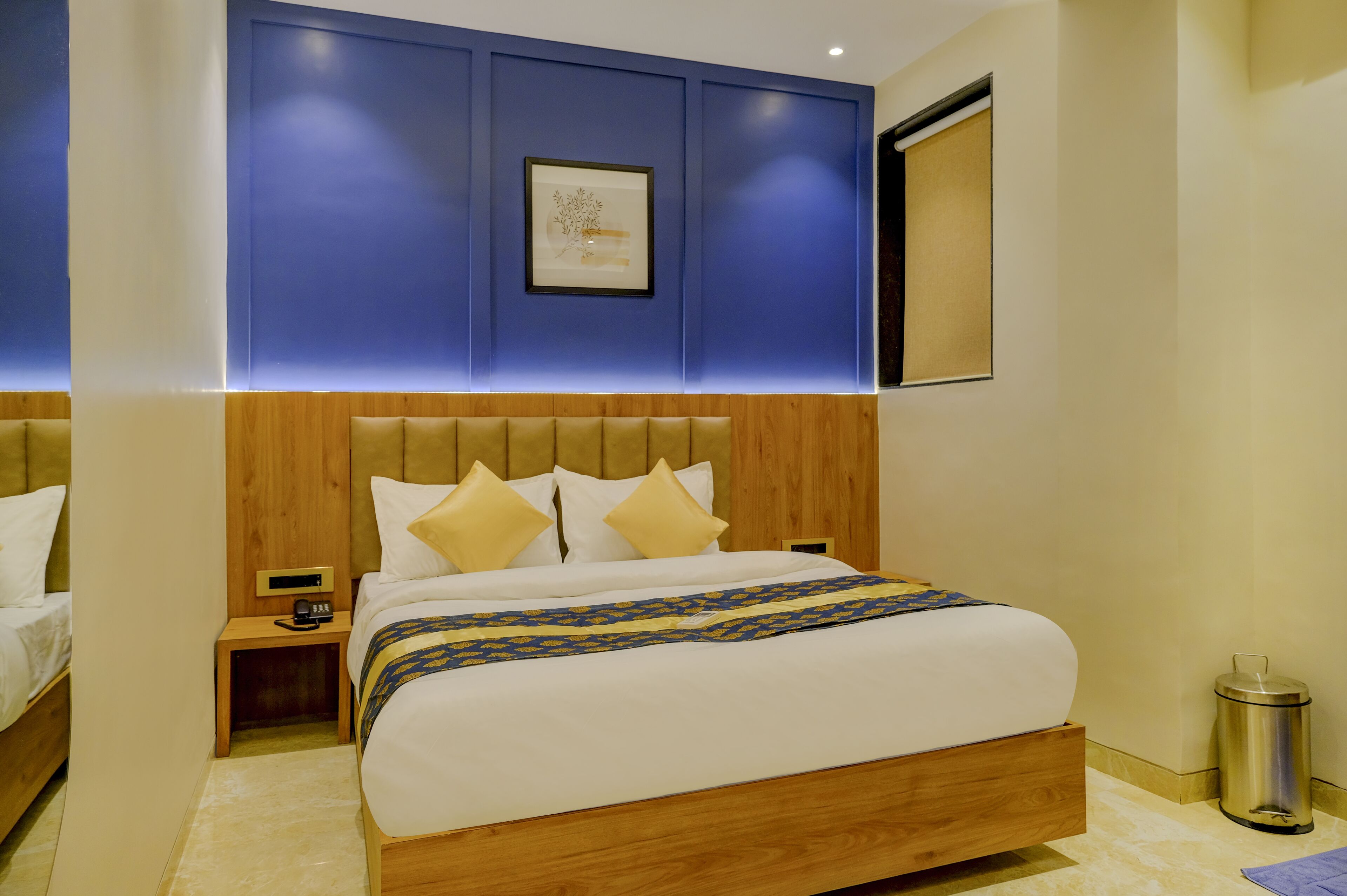Una habitación de hotel moderna con cabecera de madera, una cama grande con ropa blanca, una mesita de noche con lámpara y una obra de arte enmarcada en la pared.