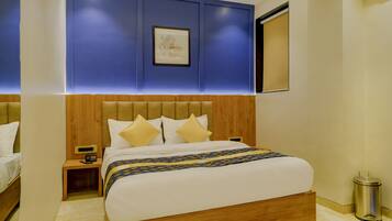 Una habitación de hotel moderna con cabecera de madera, una cama grande con ropa blanca, una mesita de noche con lámpara y una obra de arte enmarcada en la pared.