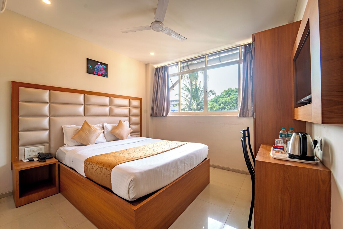 A hotel room with a bed, bedside table, and a window with curtains.