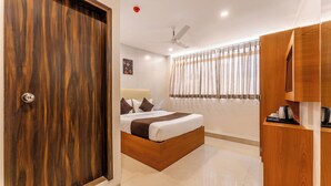 A bedroom with a wooden bed, a ceiling fan, a window with curtains, and a wooden wardrobe. - Metropolis Business Hotel (Panaji)