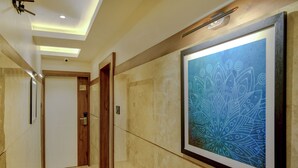 A hallway with a framed artwork, a wooden door, and a light fixture. - Metropolis Business Hotel (Panaji)