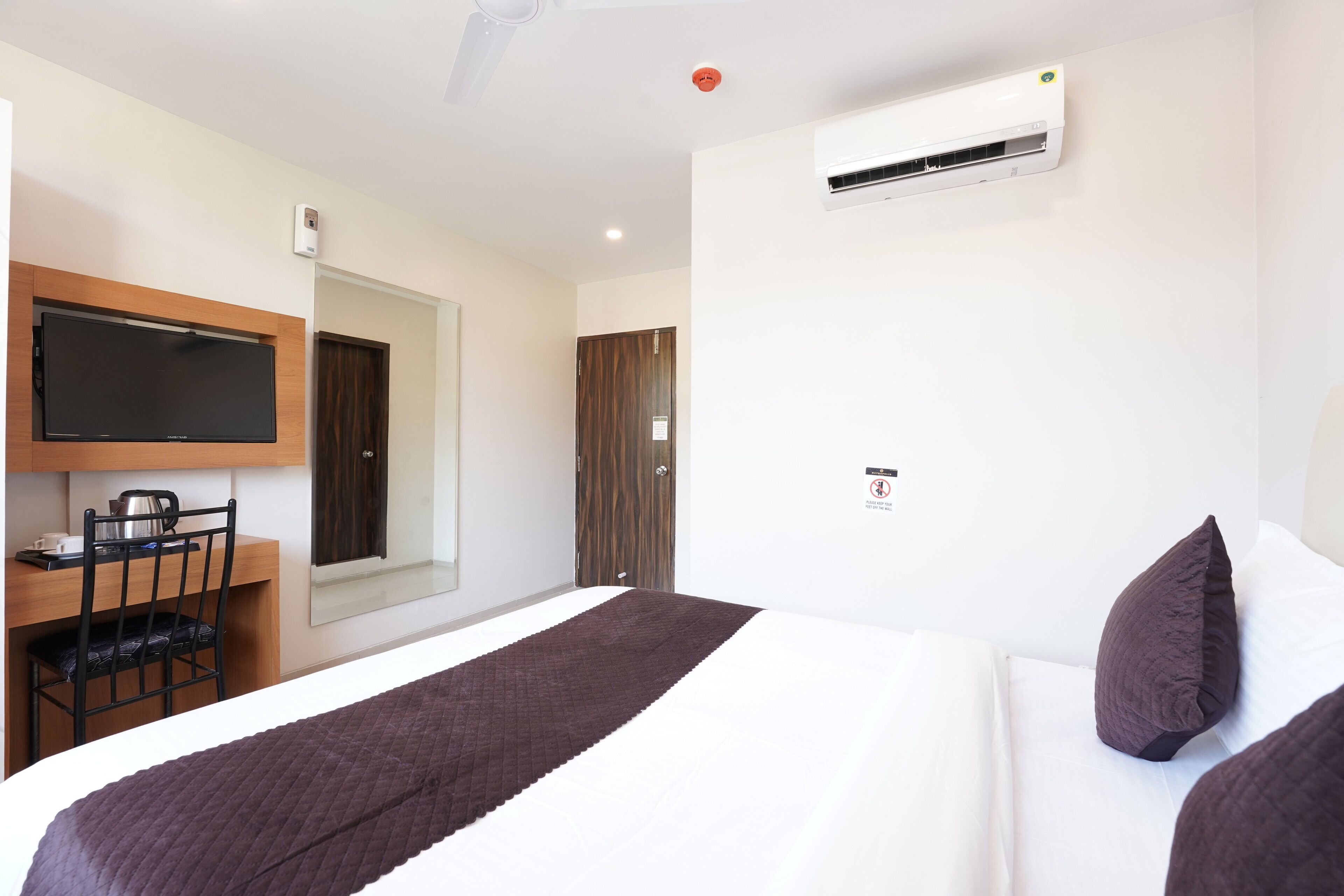 A hotel room with a bed, a desk with a chair, a television, and an air conditioning unit.