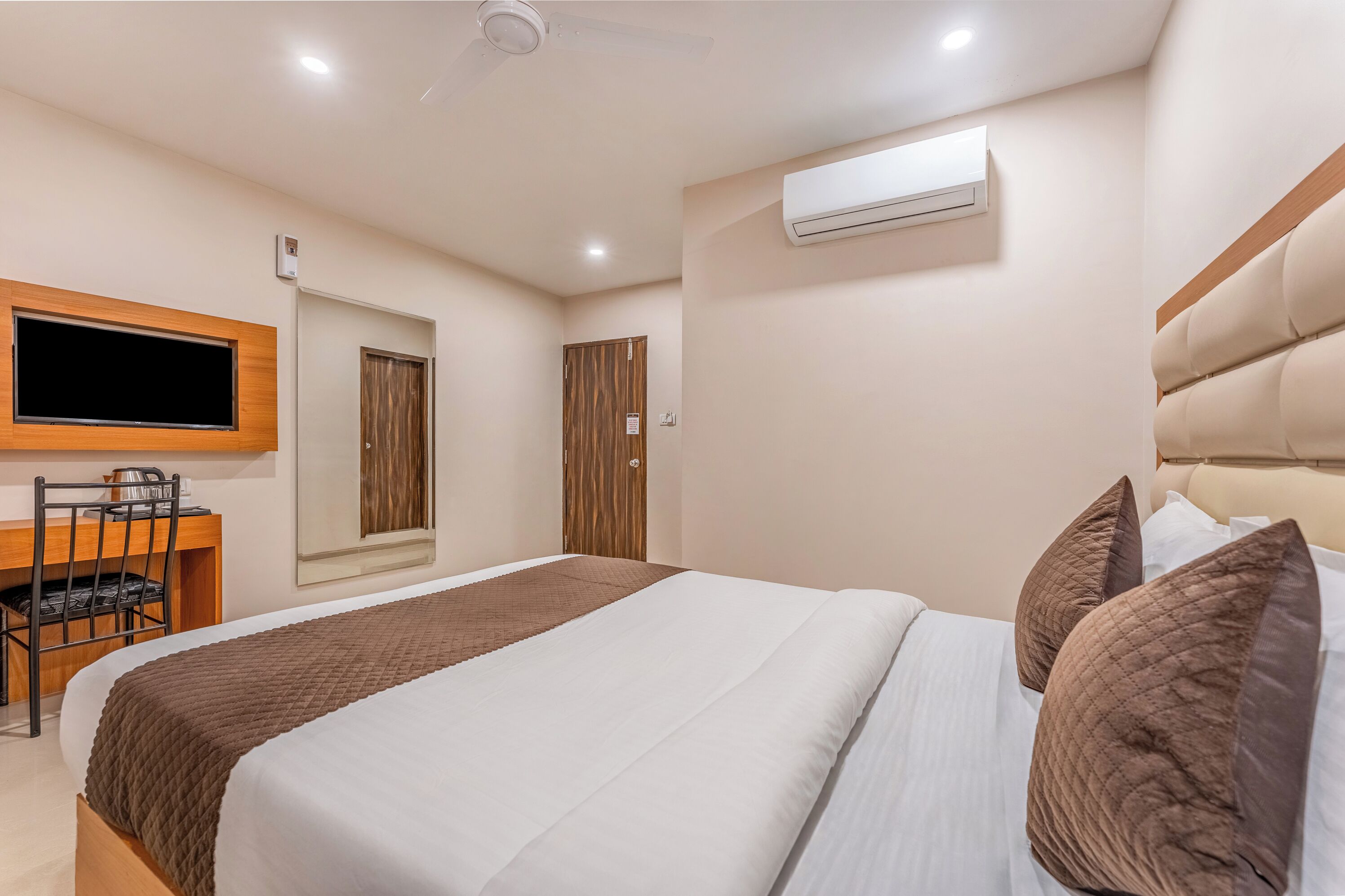 Een hotelkamer met een bed, bureau, stoel, televisie en een airconditioning.