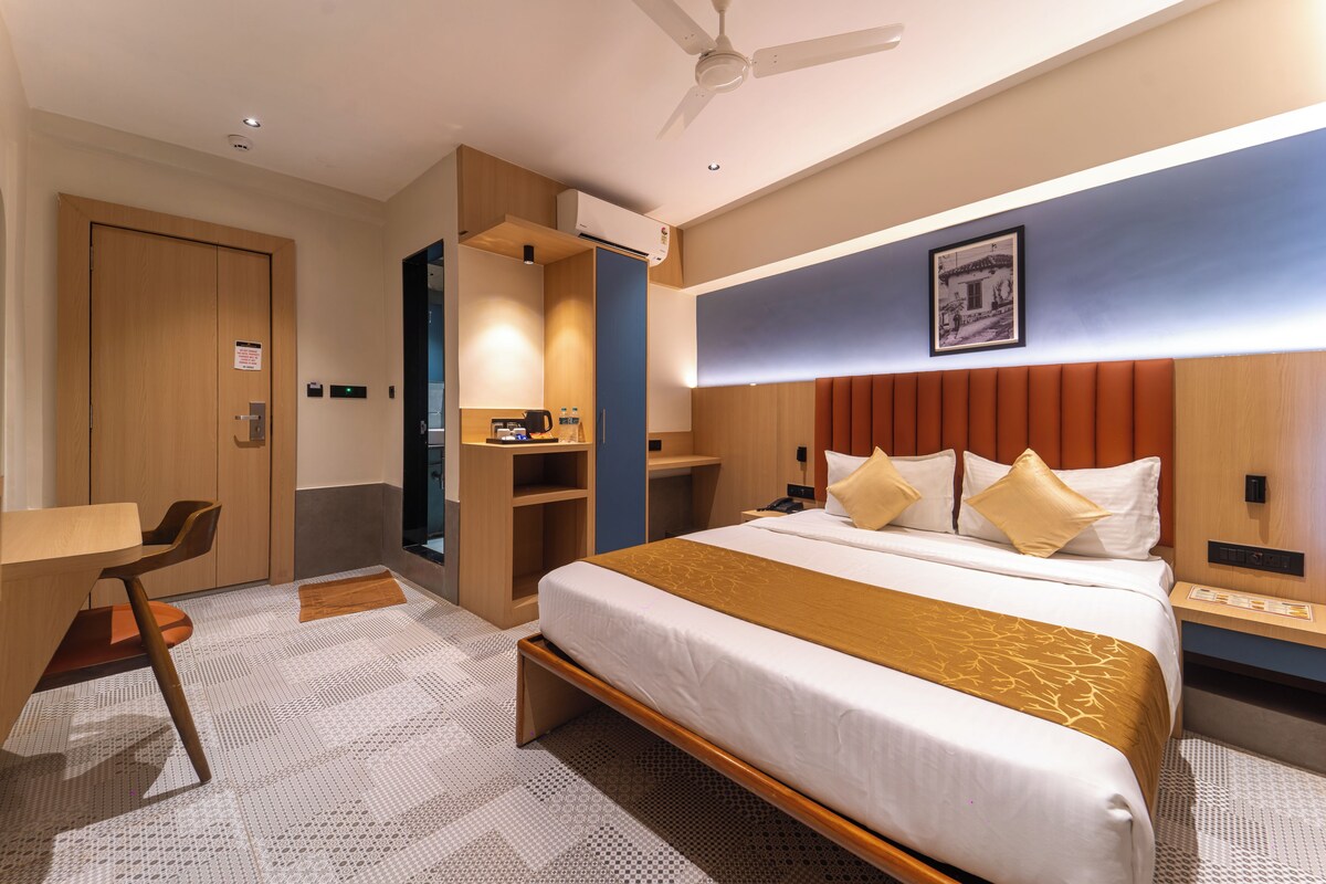 A hotel room with a bed, bedside tables, a desk, a chair, a wardrobe, and a ceiling fan.