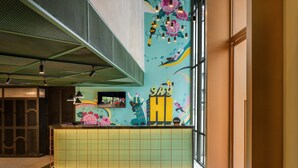 Un espace d’accueil moderne agrémenté d’une fresque colorée, d’un comptoir de réception et d’un plafond haut orné d’un motif en réseau.
