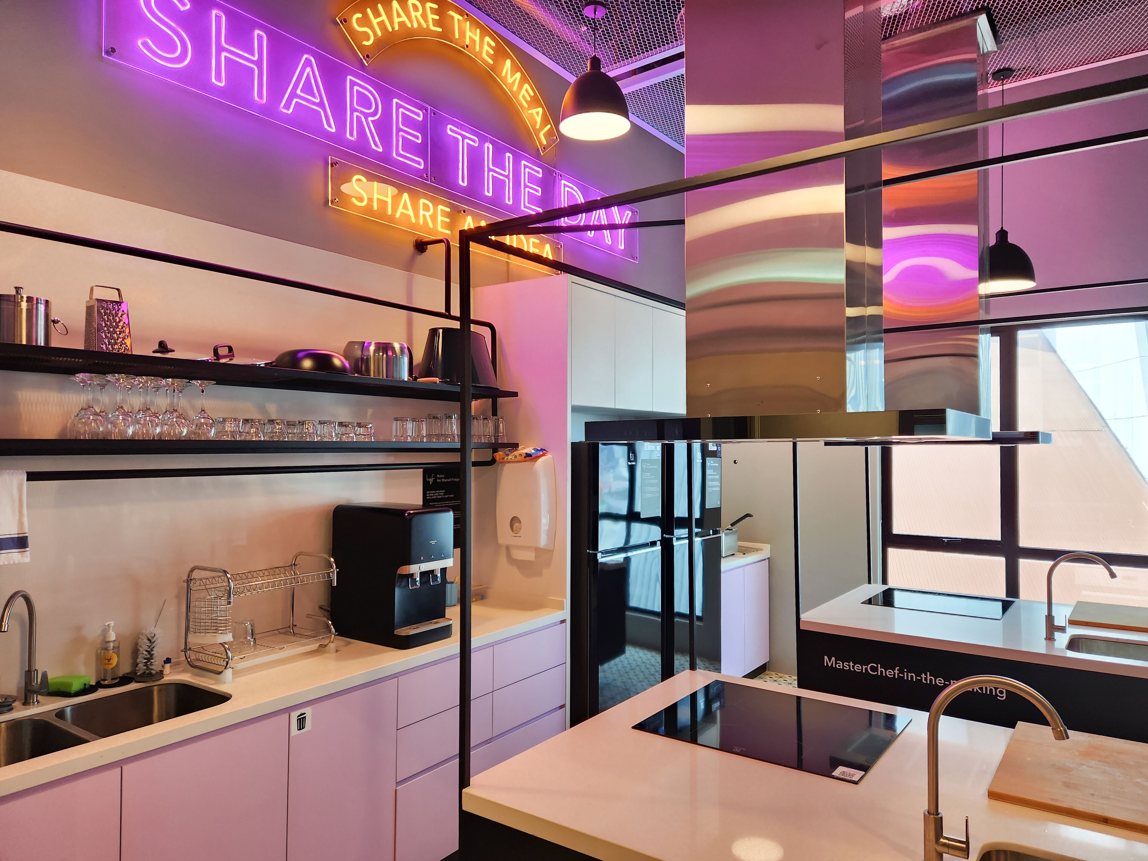 A modern kitchen with a neon sign that reads "SHARE THE MEAL SHARE THE IDEA".