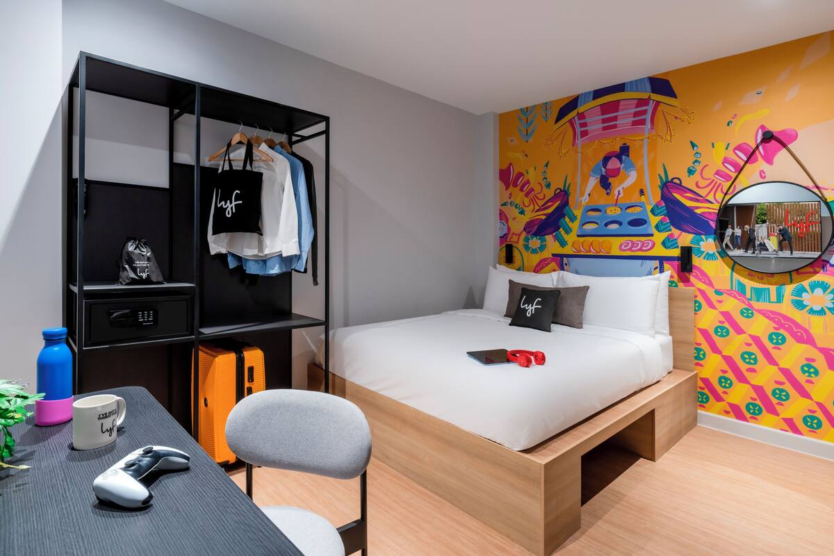 A modern bedroom with a bed, a desk with a chair, a wardrobe, and a colorful mural on the wall.