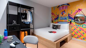 A modern bedroom with a bed, a desk with a chair, a wardrobe, and a colorful mural on the wall.