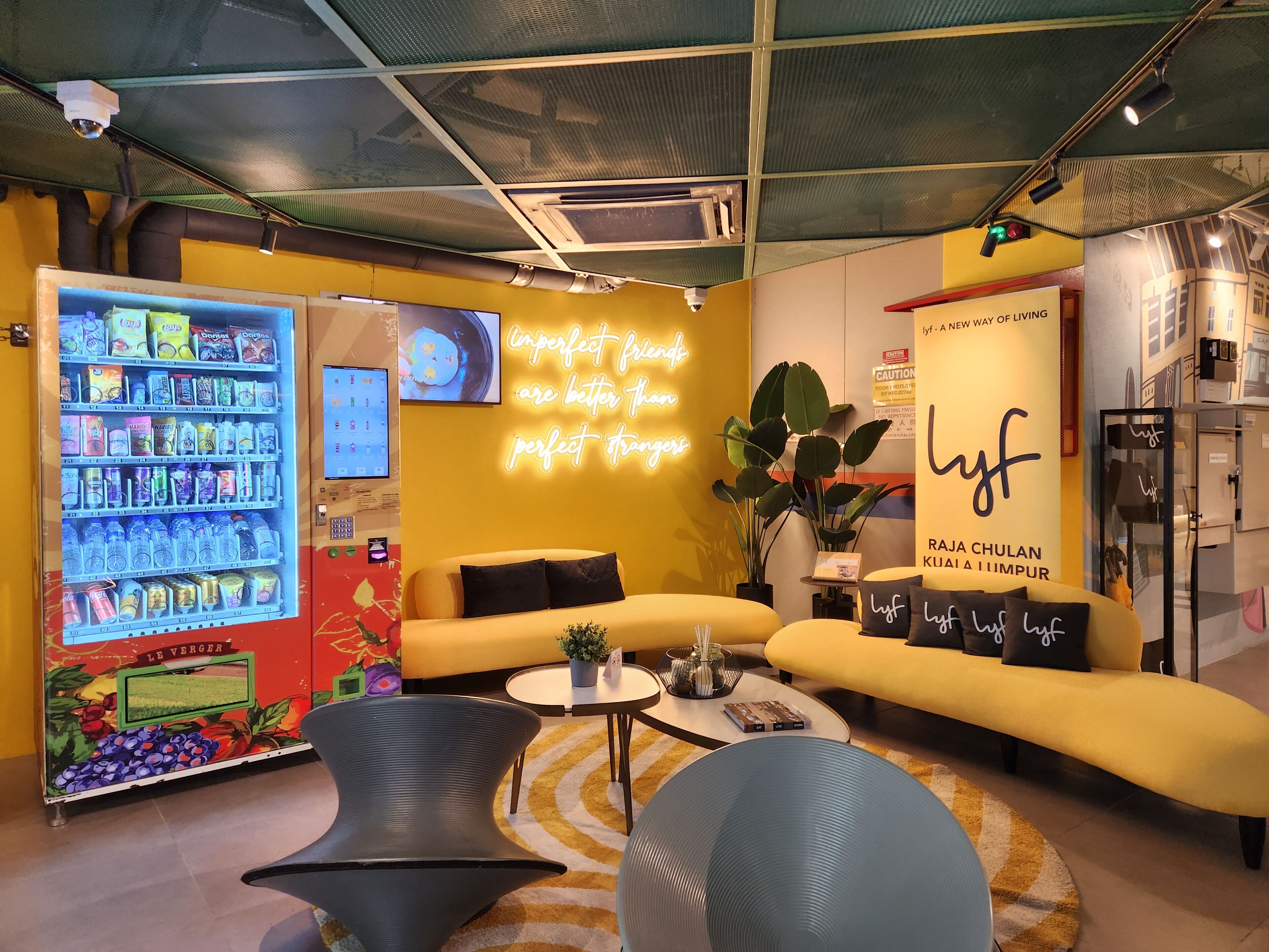 A modern lounge area with a vending machine, comfortable seating, and a neon sign.
