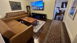 Een woonkamer met een bruine leren bank, een houten salontafel, een flatscreen televisie en een open haard.