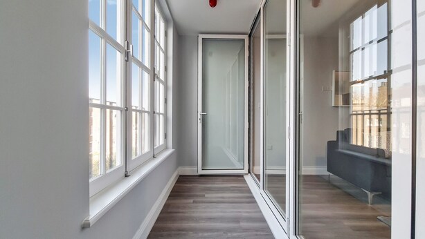 A narrow hallway with large windows on one side and a sliding glass door leading to a balcony. - Roomspace Apartments - Brewers Lane (Richmond)