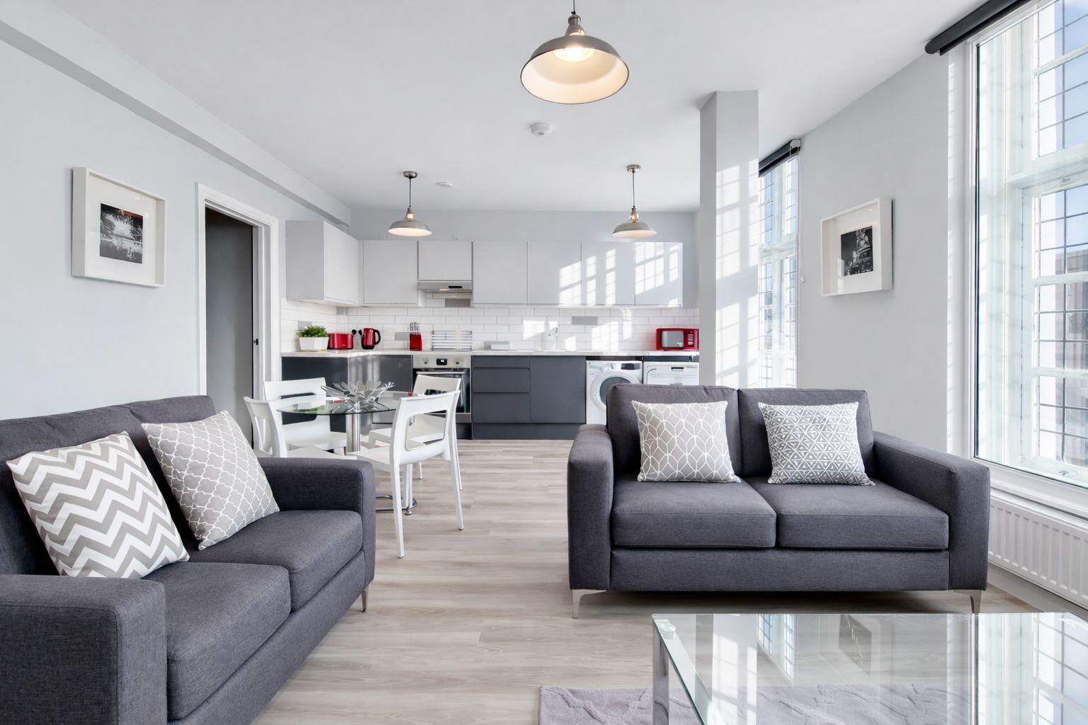 A modern living room with a sofa set, a glass coffee table, and a kitchen in the background.