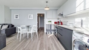 A modern kitchen with white cabinets, a stainless steel range hood, and a built-in washing machine. - Roomspace Apartments - Brewers Lane (Richmond)