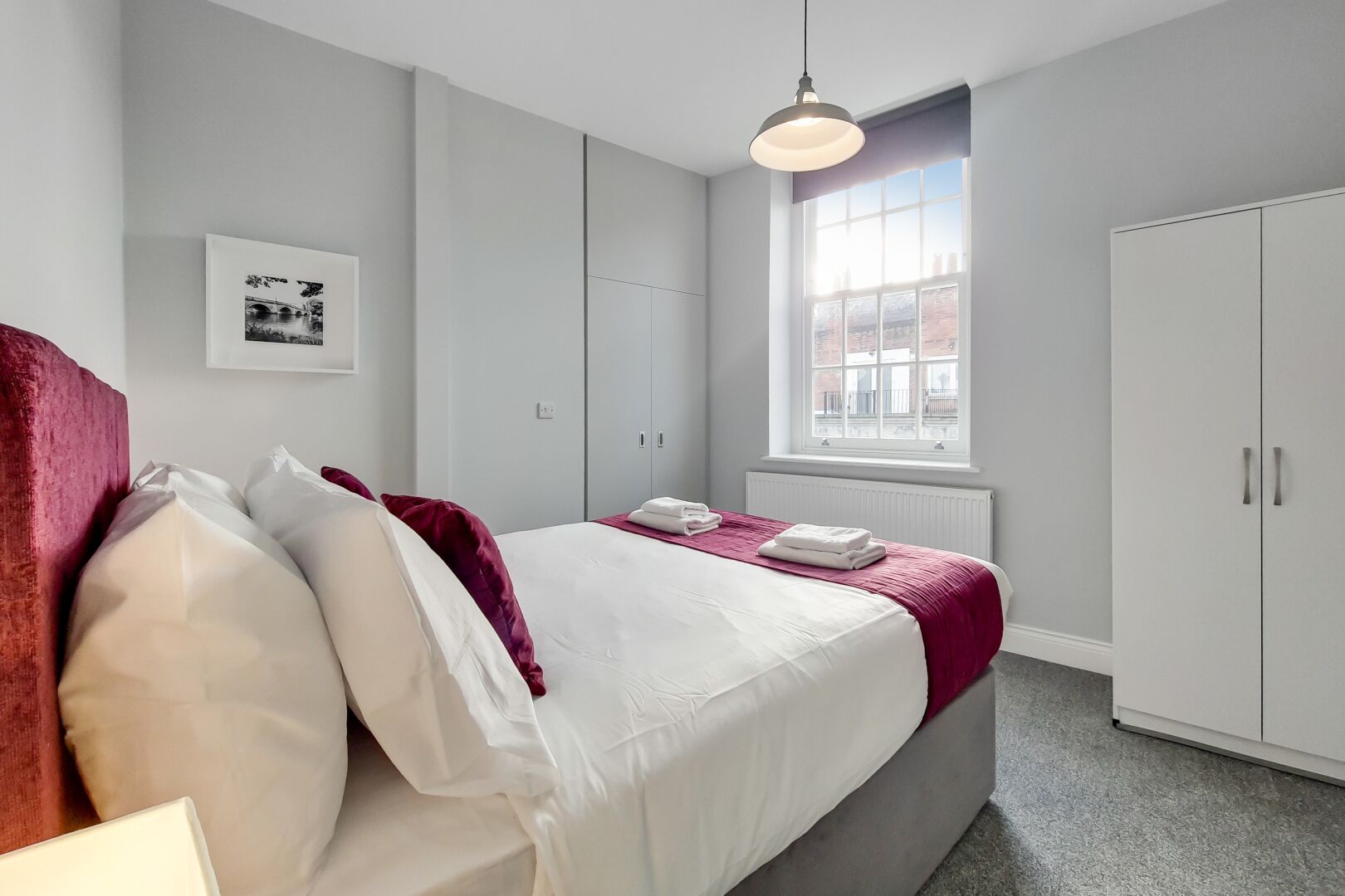 A bedroom with a bed, a window, a radiator, and a wardrobe.