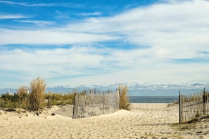 Ein sandiger Strand mit Holzlattenzaun und spärlicher Vegetation.