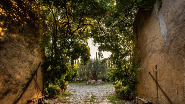 Une cour pavée de pierres, agrémentée de bancs et d’arbres, et entourée de murs en pierre.