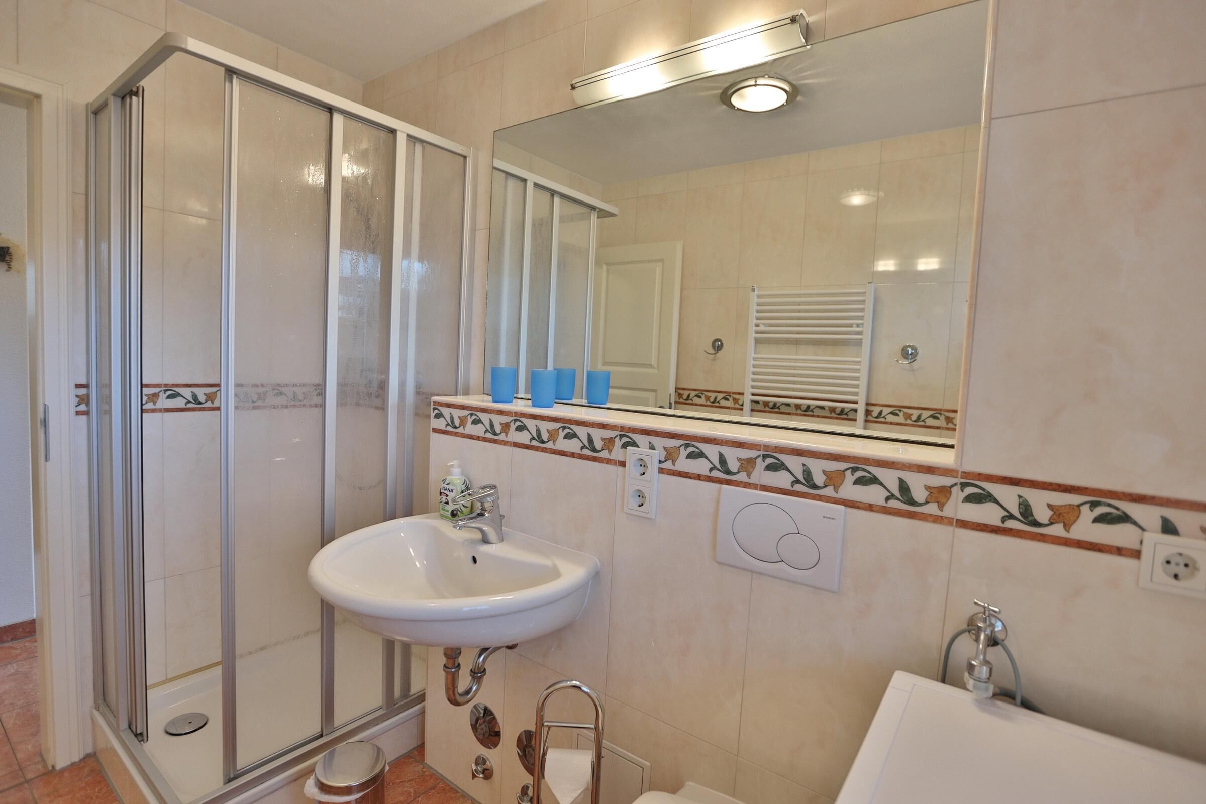 Un bany amb una cabina de dutxa de vidre, un lavabo, un mirall i un escurapous.