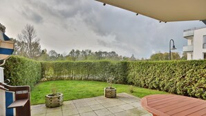 Un patio con una mesa y sillas de madera, un pequeño jardín con plantas en macetas y un seto.