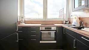 Una cucina moderna con mobili neri, elettrodomestici in acciaio inossidabile, un lavello doppio e una finestra con vista su gru da cantiere.