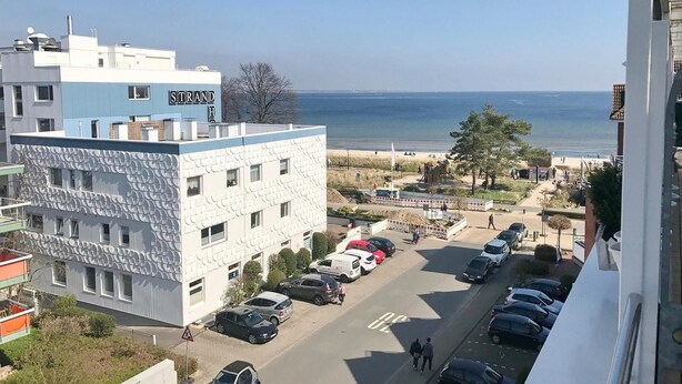 Un edificio sul lungomare con vista sul mare, un'area di parcheggio e un percorso pedonale.
