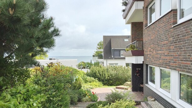 Een woongebouw met een bakstenen gevel, grote ramen en een tuin met diverse planten en een pad.