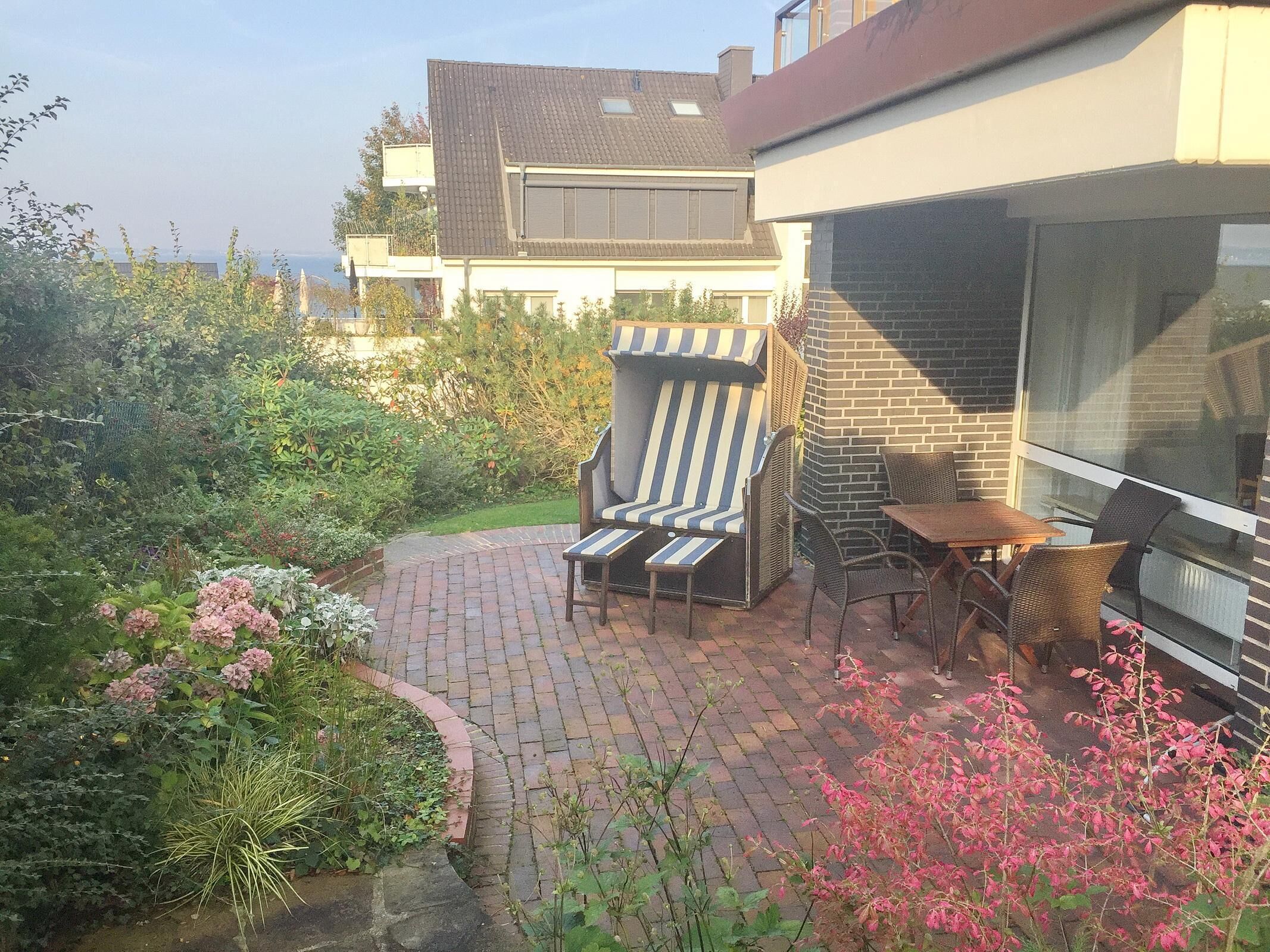 A patio with a striped lounge chair, a small table, and wicker chairs.