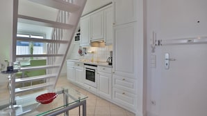A modern kitchen with white cabinetry, a glass railing, and a dining area visible through an open door. - Hansa-residenz I Appartement 17 Kumweer (Scharbeutz)