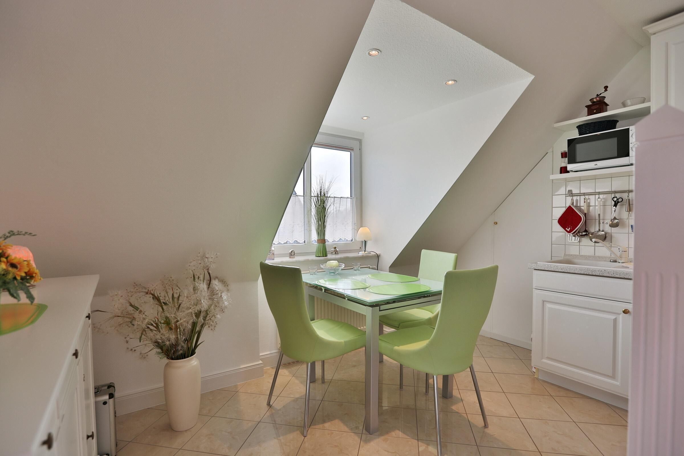 Una cocina moderna con comedor, que incluye una mesa de vidrio, sillas verdes y un armario blanco con microondas.